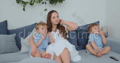 妈妈抱着两个小儿子在客厅的沙发上看电视.. 家庭看电视